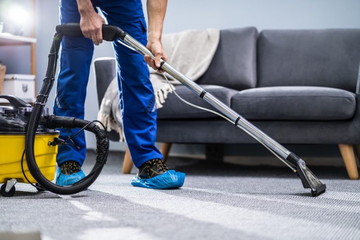Professional cleaner vacuuming carpet in a living room using industrial cleaning equipment, removing dirt and allergens for a fresh, clean home