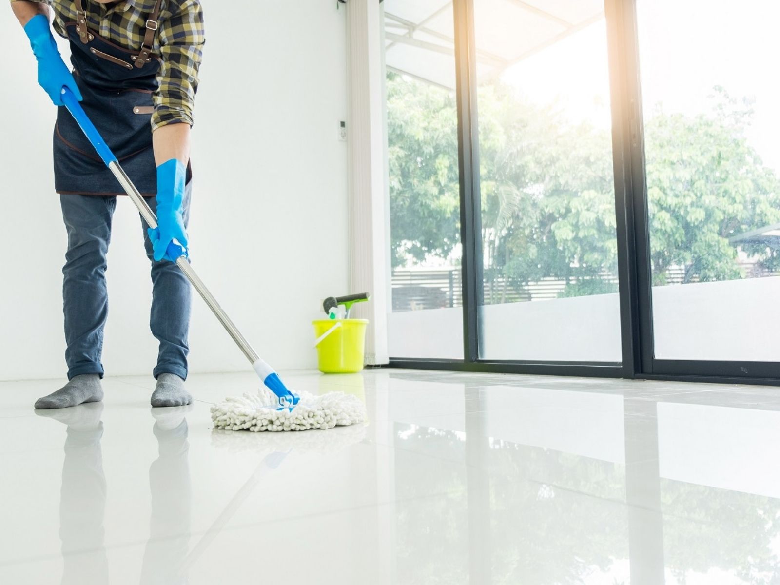 Worker cleaning a smooth white floor using a mop, with a bucket in the background.